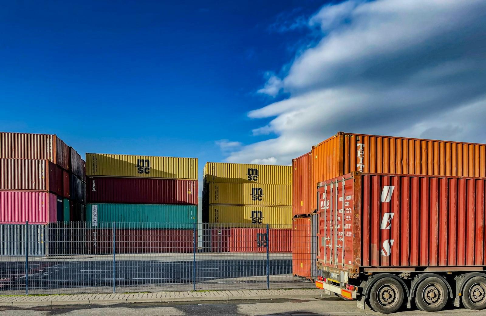 A truck parked in front of stacked shipping containers in a container yard